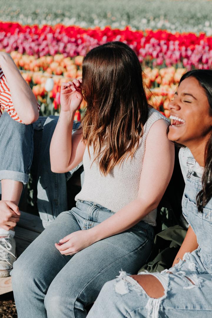 Drei Freundinnen sitzen auf einer Bank vor einem Tulpenfeld und lachen