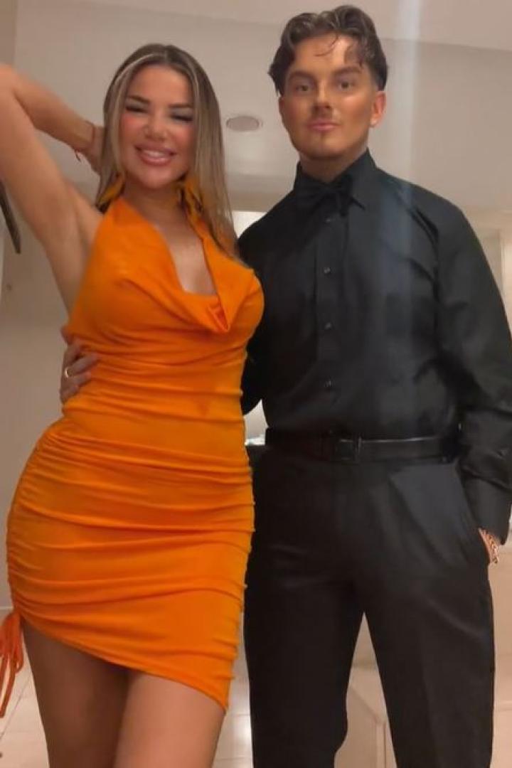 Frau in einem orangenfarbenen Kleid posiert neben einem Mann in schwarzem Anzug