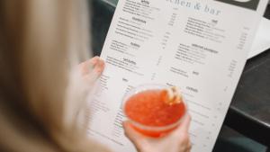 Blonde Frau hat einen Drink in der rechten und eine Speisekarte in der linken Hand