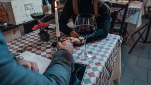 Pärchen sitzt an einem Tisch mit einer karierten Tischdecken und einem Glas Wein. Sie halten sich an den Händen