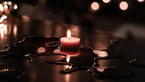 Rote Kerze brennt auf einem schwarzen Tisch. Rundherum sieht man geschmolzenes Wachs. 