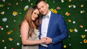 Sommerhaus der Stars-Teilnehmer Justine Dippl und Arben Zekic posieren vor eine grünen Wand mit einzelnen Blüten