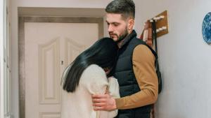 Schwarzhaarige Frau kuschelt sich mit verdecktem Gesicht an Mann