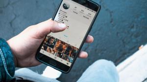 Männerhand hält Smartphone in der Hand mit einem Profil eines Instagram-Users auf dem Screen