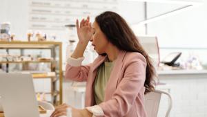 Frau sitzt vor Laptop und dreht sich weg, um zu husten.