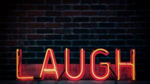 Ein Neonschild, welches das Wort "Laugh" in orange zeigt.