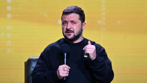 Wolodymyr Selenskyj sitzt vor einer gelben Leinwand und hält ein Mikrofon