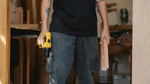 Mann mit gelbem Akkuschrauber und Holscheitel in der Hand