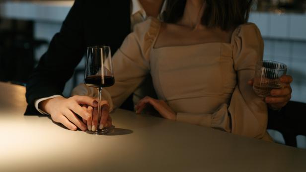 Pärchen schmiegt sich in einer Bar aneinander und halten ein Glas Wein fest