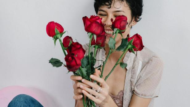 Frau hält Strauß roter Rosen in den Händen und strahlt über das ganze Gesicht