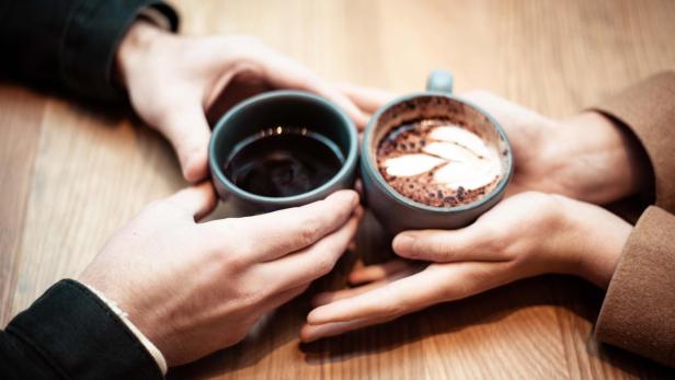 Zwei Hände halten zwei kaffeebecher auf einem Holztisch