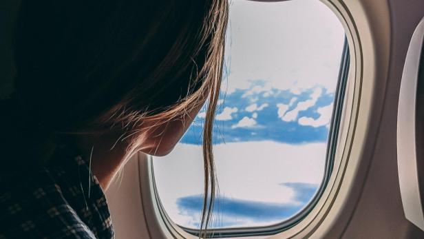 Frau hält ein Handy in der Hand und blickt aus dem Flugzeugfenster