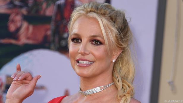 Britney Spears lächelt in die Kamera während sie ihre Hand hebt