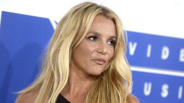Britney Spears blickt nach rechts und steht vor einer blauen Werbewand.