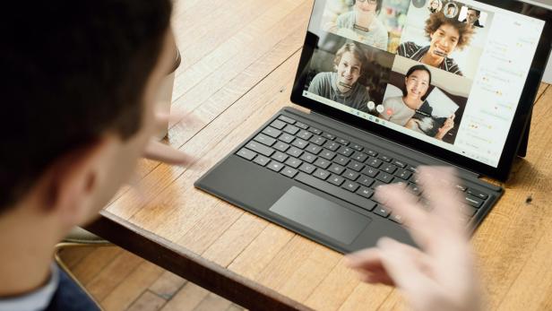 Mann blickt auf Laptop, auf dessen Bildschirm vier Teilnehmern eines Online-Meetings zu sehen sind