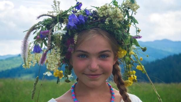 Junges Mädchen mit Blumen im Haar auf einer Wiese.