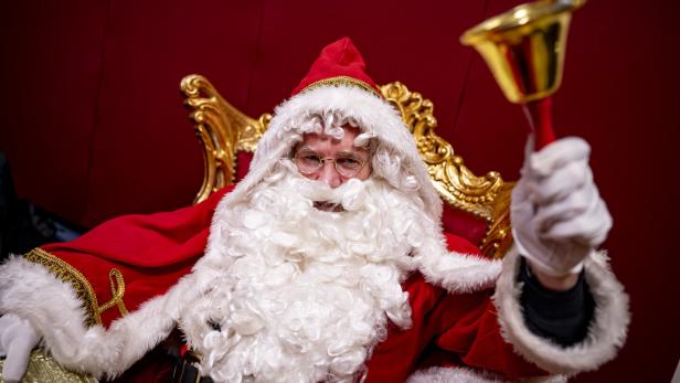 Weihnachtsmann mit Bart und Glocke in der Hand sitzt auf einem goldenen Thron.
