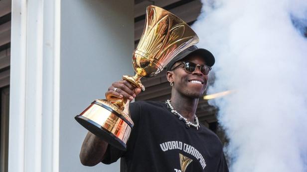 Dennis Schröder hält einen Pokal in der Hand und lächelt. 