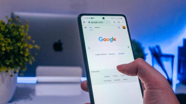 Hand hält Smartphone, auf dessen Display die Google-Startseite zu sehen ist