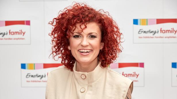  No-Angels-Sängerin Lucy Diakovska steht vor einer Erstings Family Werbewand und lächelt in die Kamera