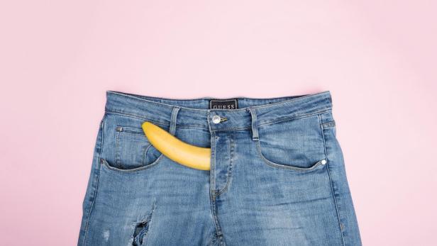 Banane lugt aus Hosentür einer Jeans vor rosa Hintergrund