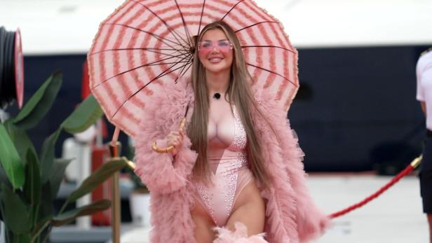 Kim Virginia in einem rosa Body, rosa Mantel und einem gleichfarbigen Regenschirm