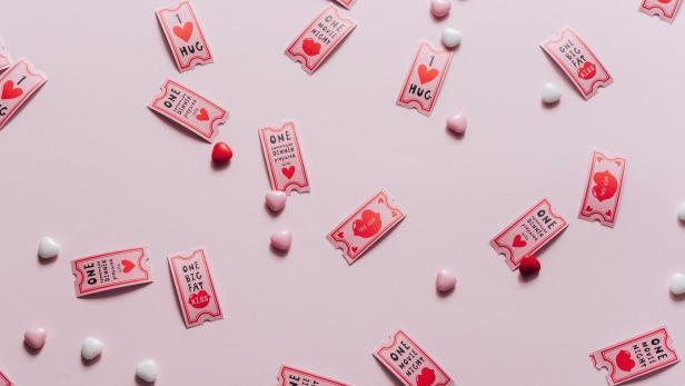 Kleine Zettel mit Liebesbotschaften liegen zusammen mit Zuckerherzen auf rosa Hintergrund