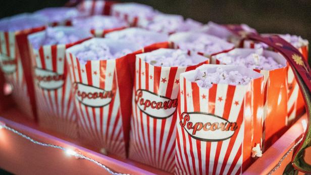 Mehrere Tüten Popcorn mit weiß-roten Streifen und der Aufschrift Popcorn in einem roten Tablet mit einer Lichterkette