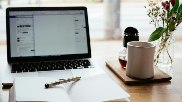 Ein Laptop, Notizbuch und Tee auf einem Schreibtisch