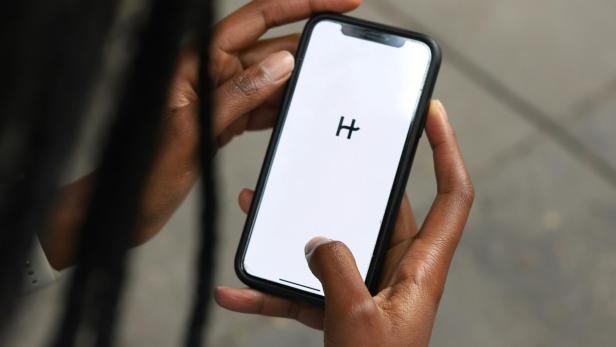 Smartphone mit weiß leuchtendem Bildschirm und dem schwarzen Buchstaben H wird in Händen gehalten
