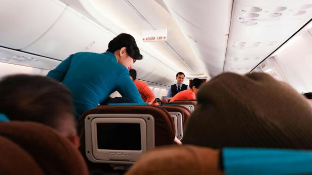 Flugbegleiterin mit blauem Kostüm geht in einem Flugzeug durch die Reihen