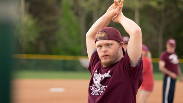 Junger Mann mit Down-Syndrom streckt steht auf dem Sportplatz und streckt seine Arme in die Luft.