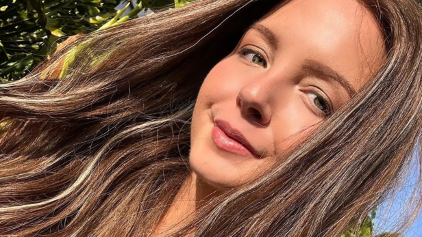 Brünette 26-jährige Frau mit grünen Augen lächelt für ein Selfie in die Kamera